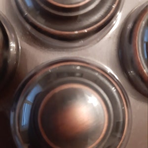 Może przedstawiać: Cztery okrągłe, ozdobne, miedziane uchwyty do szuflad z wzorem koncentrycznych k&oacute;ł.