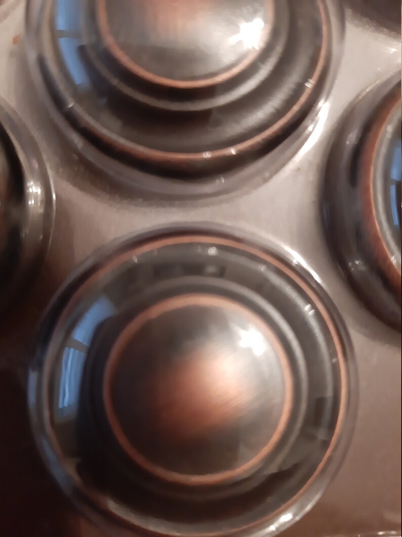 Może przedstawiać: Cztery okrągłe, ozdobne, miedziane uchwyty do szuflad z wzorem koncentrycznych k&oacute;ł.