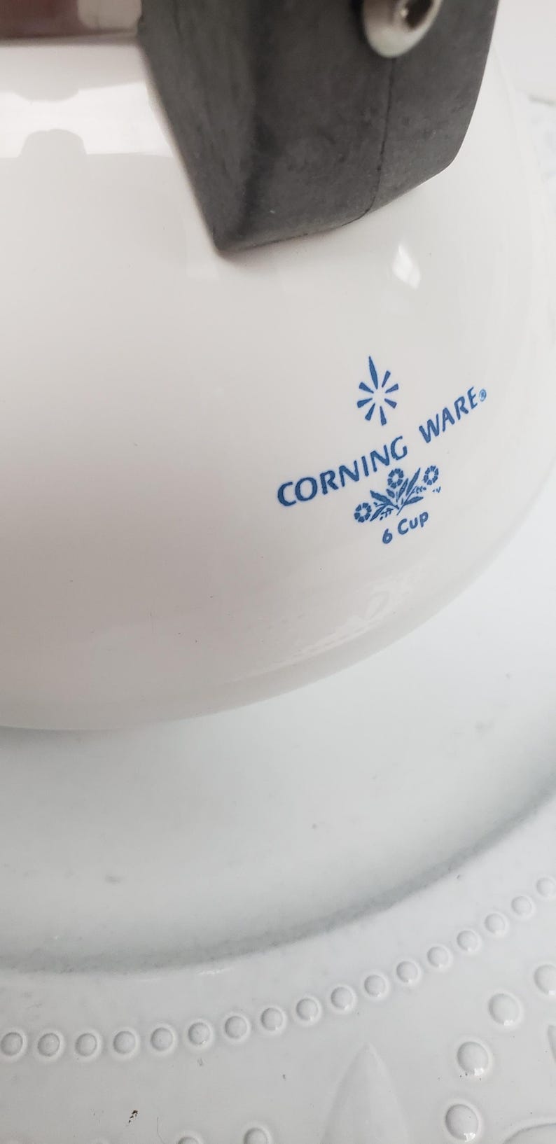 Op de afbeelding: Witte Corning Ware 6-kops ovenschaal met blauwe tekst en een bloemenmotief.