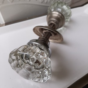 Pode incluir: Um par de maçanetas de porta de vidro vintage com acabamento prateado. As maçanetas são redondas e têm um design facetado.