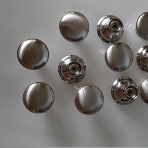 K&ouml;nnte beinhalten: Zehn silberne Schrankkn&ouml;pfe mit runder, flacher Oberseite und einem erh&ouml;hten, runden Sockel. Die Kn&ouml;pfe haben eine gl&auml;nzende, polierte Oberfl&auml;che.