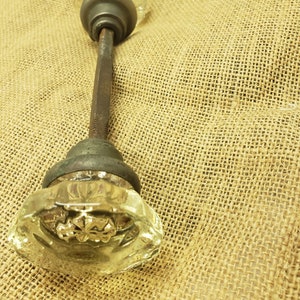 Pode incluir: Uma maçaneta de porta de vidro vintage com um design de vidro transparente e uma base de metal. A maçaneta está presa a uma haste de metal.