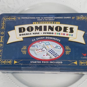 Może przedstawiać: Niebieskie pudełko z domino z napisem "Collectors Dominoes Double Nine Jumbo Color Dot" i "55 Shiny Dominoes". Pudełko zawiera również instrukcje do 16 różnych gier w domino.