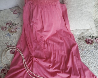 May include: A pink sleeveless nightgown with a lace trim around the neckline and a satin trim around the bottom. The nightgown is laying on a white floral patterned bedspread with a string of pearls.