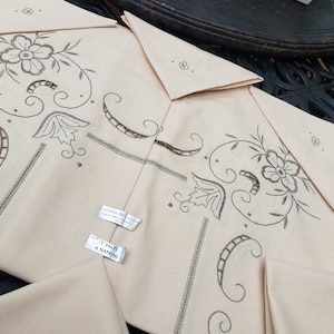 Pode incluir: Conjunto de seis guardanapos de algodão de cor creme com desenhos florais bordados. Os guardanapos têm uma borda festonada e são feitos de 100% algodão. O rótulo diz "Cotton 100% Cotton" e "1 54x72 6 Napkins".