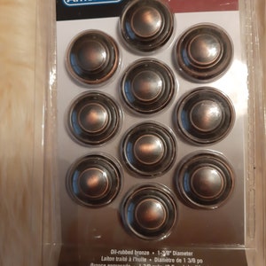 Op de afbeelding: Tien kastknoppen van olie-gebronsd brons met een diameter van 3,5 cm. De knoppen hebben een concentrisch cirkelontwerp. De verpakking bevat de productcode BP1586-ORB.