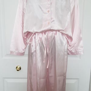 May include: A pink satin pajama set with long sleeves and pants. The top has a button-up front and a collar. The pants have a drawstring waist.