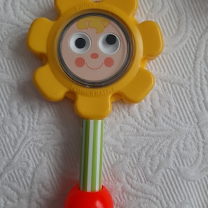 May include: A vintage Fisher-Price Flower Rattle toy. The yellow flower-shaped head features a smiling face and the text "FLOWER RATTLE". The handle is green and white striped, with a red ball at the base. A classic baby toy.