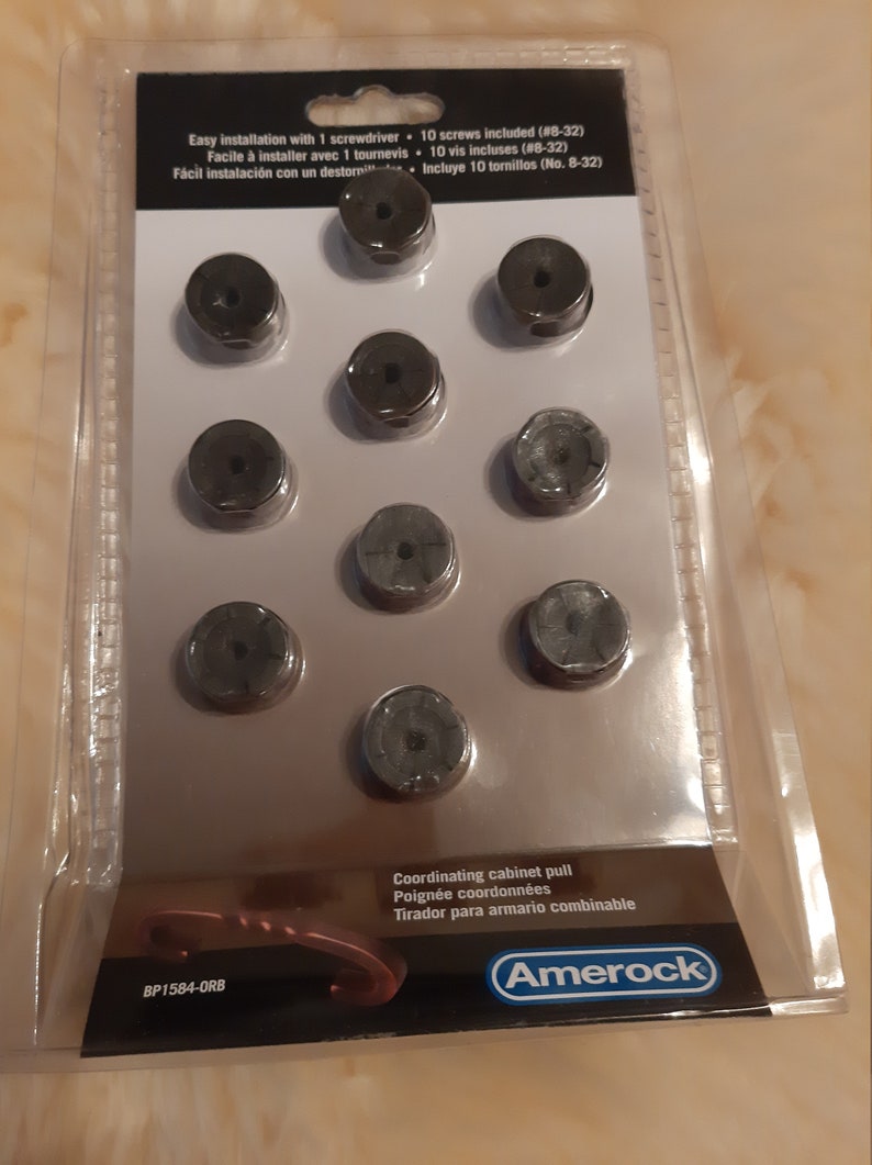 Może przedstawiać: Opakowanie dziesięciu czarnych gałek do szafek z dopasowaną gałką do szafki. Opakowanie zawiera 10 śrub do łatwego montażu. Opakowanie jest oznaczone "Amerock" i "BP1584-ORB".