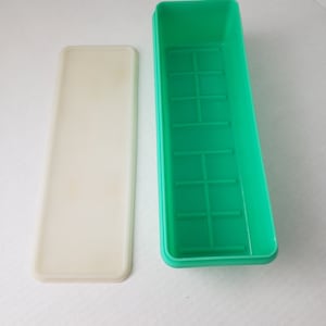 May include: A green plastic rectangular container with a white lid. The container has a grid pattern inside.