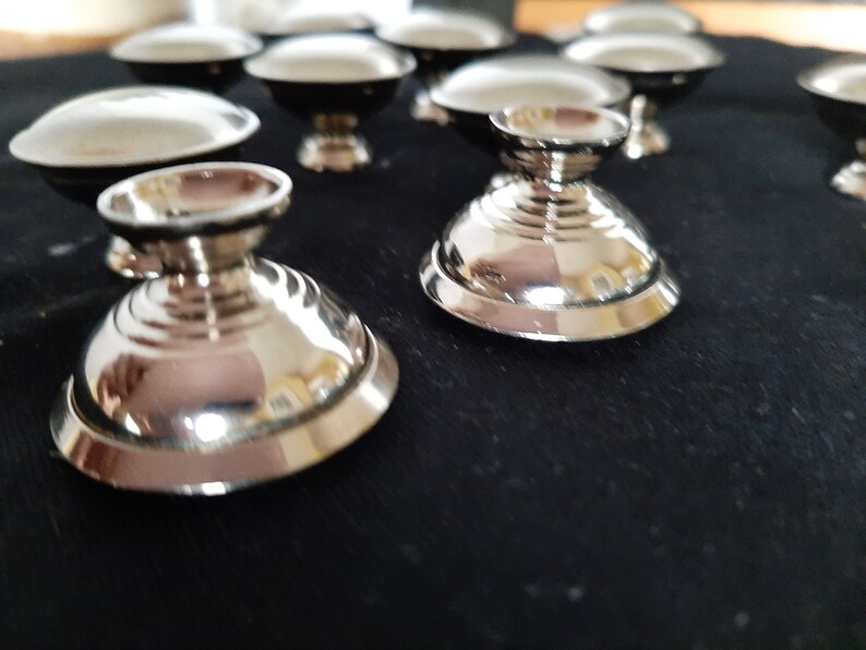 K&ouml;nnte beinhalten: Ein Satz silberfarbener, dekorativer Schalen mit runder Basis und erh&ouml;htem Rand. Die Schalen sind in einer Reihe auf einer schwarzen Oberfl&auml;che angeordnet.