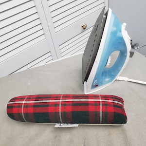 May include: A red and black tartan ironing board cover with a white label. The cover is on a grey surface next to a blue and grey iron.