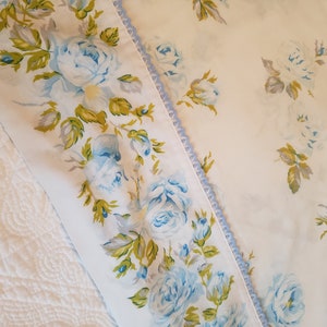 May include: A white fabric with a blue floral pattern. The fabric has a blue lace trim along one edge.