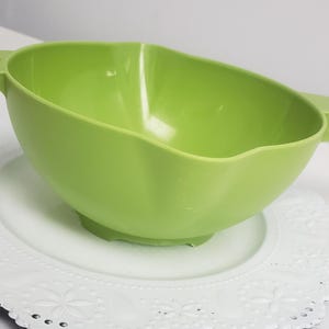 May include: A bright green plastic colander with a handle, sitting on a white lace doily.