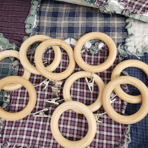May include: A set of ten wooden curtain rings with silver clips. The rings are light brown and have a smooth finish. The clips are attached to the rings and are used to hold curtains in place.