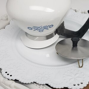 Op de afbeelding: Witte theepot met een blauw bloemenmotief en een zwarte handgreep. De theepot staat op een wit kantje.