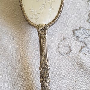 May include: A silver hand mirror with an ornate handle and a floral design etched into the surface.