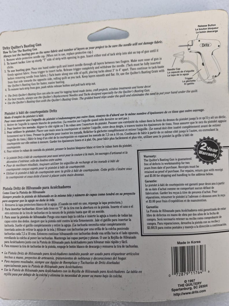 May include: A Dritz Quilter's Basting Gun packaging card featuring detailed instructions in English, French, and Spanish. The card includes a diagram of the tool, a 2-year warranty seal, a barcode, and manufacturing information printed on white paper.