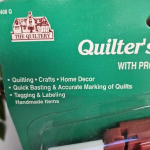 May include: A green product packaging card for The Quiltery Quilter's tool. The text lists uses including quilting, crafts, home decor, quick basting, accurate marking of quilts, and tagging and labelling handmade items. The card is partially visible.