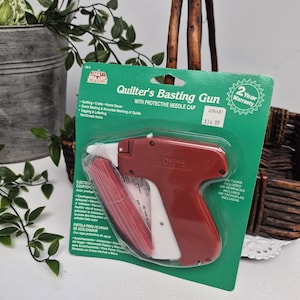 Puede incluir: Una pistola de hilvanar para acolchado marca Dritz con tapa protectora de aguja, en un empaque de cartón verde. La herramienta roja y blanca está diseñada para acolchados y manualidades, e incluye 500 tachuelas para marcar y etiquetar.