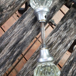 Può includere: Un paio di pomelli per porte in vetro antico con finitura argentata. I pomelli hanno un design sfaccettato e sono collegati da un'asta di metallo.