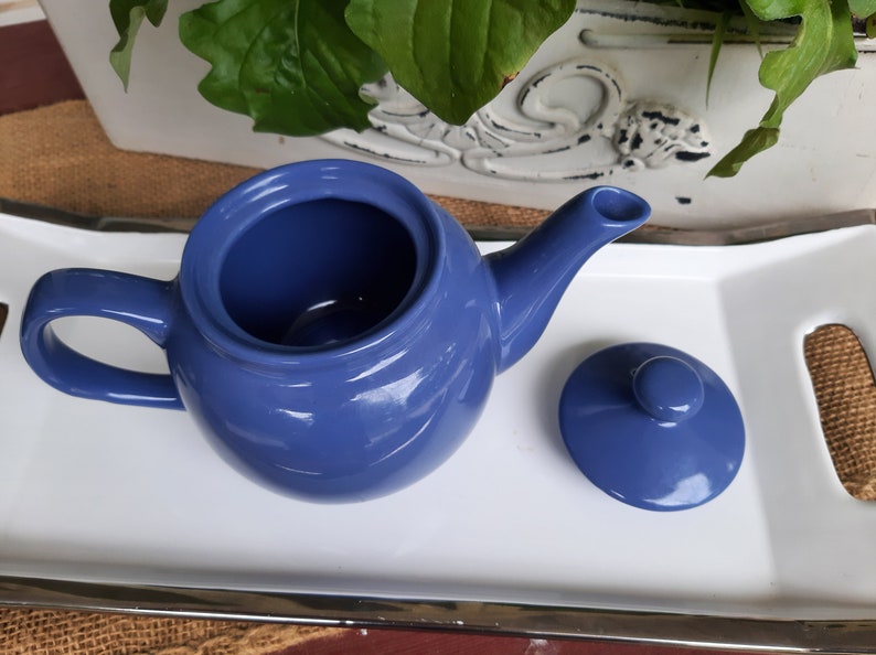 May include: A blue ceramic teapot with a matching lid. The teapot has a round body and a curved spout. The lid has a small knob on top.
