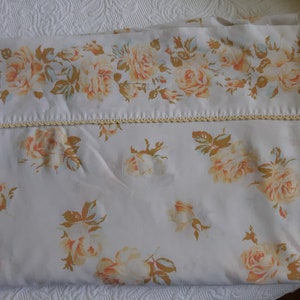 May include: A white fitted sheet with a delicate floral pattern featuring yellow and orange roses. The sheet has a crocheted trim around the edge.