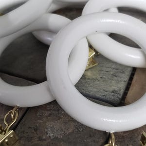 May include: White wooden curtain rings with gold clips and chains. The rings are stacked on top of each other.