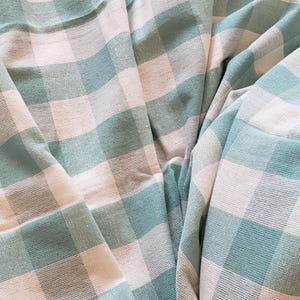 May include: A green and white gingham fabric with a soft, textured surface. The fabric is folded and draped, creating a pattern of squares.