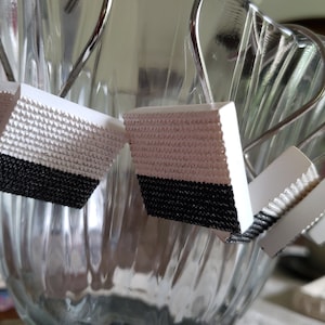 May include: Close-up of four white and black patterned clips hanging from a glass vase. The clips have a textured white top and a black bottom.