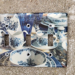 May include: A white light switch cover with a blue and white floral pattern featuring a variety of teacups, saucers, and creamer pitchers.