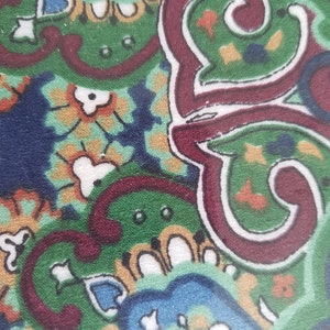 May include: A close-up of a fabric with a paisley pattern. The fabric is a mix of green, red, blue, and white. The pattern is intricate and detailed.