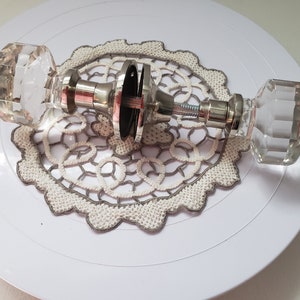 May include: A pair of crystal door knobs with a silver finish. The knobs are disassembled and laid out on a white surface.