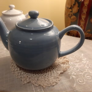 Peut inclure: Une théière en céramique bleue avec une dentelle blanche en dessous. La théière a un couvercle et une poignée.