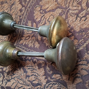 以下が含まれることがあります： 金属製のねじ付きロッドが付いたアンティークな真鍮製のドアノブ2個。ノブは丸型で、わずかにドーム型のトップがあります。