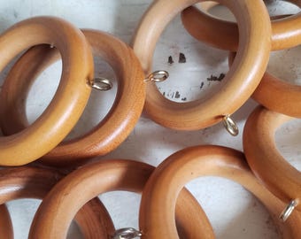 Könnte beinhalten: Ein Satz Holzvorhangringe mit goldenen Metallhaken. Die Ringe sind hellbraun und haben eine glatte Oberfläche.