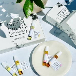 May include: A perfume sample set from Wit & West Perfumes. The set includes several small vials of perfume, each with a label. The packaging is white with a black marble design. The sample set is displayed on a white plate.