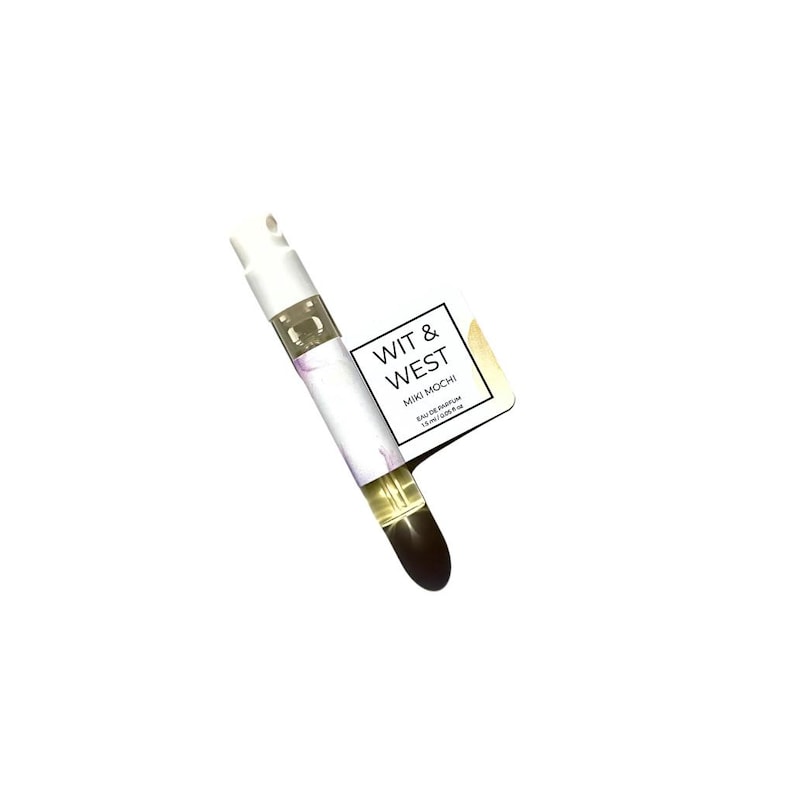 May include: A small perfume sample vial with a white cap and a clear glass body. The vial contains a light yellow liquid and is labeled "WIT & WEST MIKI MOCHI EAU DE PARFUM 1.5ml/0.05 fl oz."