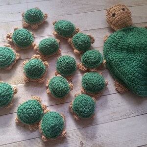 May include: A collection of crocheted green and tan turtle toys. The turtles are arranged in a line, with a larger turtle at the end. The turtles are all different sizes and have different facial expressions.