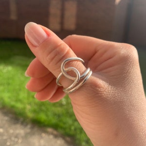Op de afbeelding: Een zilveren ring met een uniek, verweven ontwerp. De ring wordt gedragen op de duim.