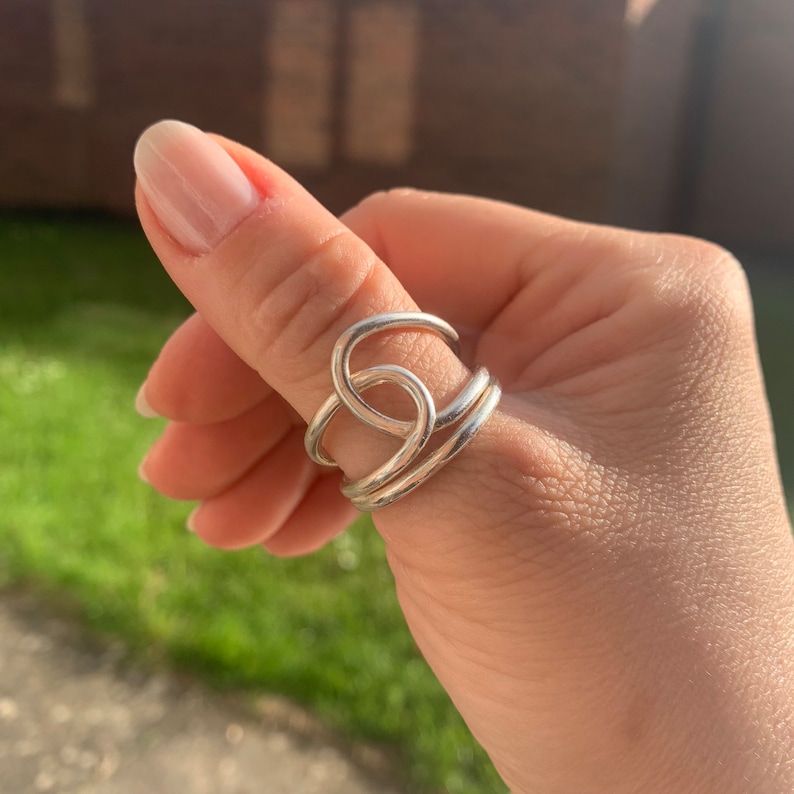 Op de afbeelding: Een zilveren ring met een uniek, verweven ontwerp. De ring wordt gedragen op de duim.
