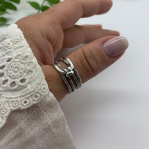 May include: A silver ring with a textured design. The ring is made of multiple bands that are connected by a small, decorative piece.