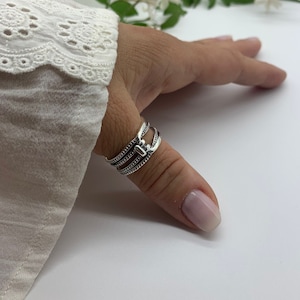 May include: A silver thumb ring with a textured design. The ring is made of multiple bands that are stacked on top of each other.