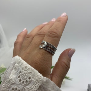 May include: A silver ring with three bands, each with a beaded design. The bands are connected by a small, decorative piece.