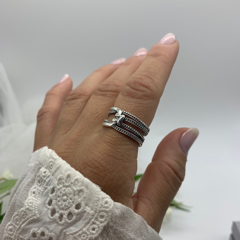 May include: A silver ring with three bands, each with a beaded design. The bands are connected by a small, decorative piece.