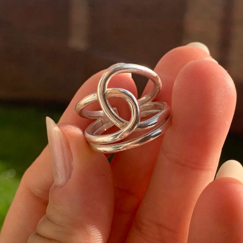 Op de afbeelding: Een zilveren ring met een uniek, verweven ontwerp. De ring is gemaakt van drie banden die gedraaid en met elkaar verweven zijn om een complex en interessant patroon te cre&euml;ren.