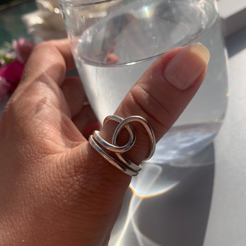 Op de afbeelding: Een zilveren ring met een knoopontwerp. De ring wordt op de duim gedragen.