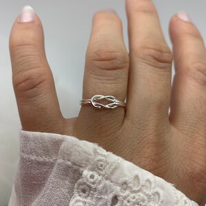 Op de afbeelding: Een zilveren knoop ring met een eenvoudig ontwerp. De ring wordt gedragen op de middelvinger van een hand.