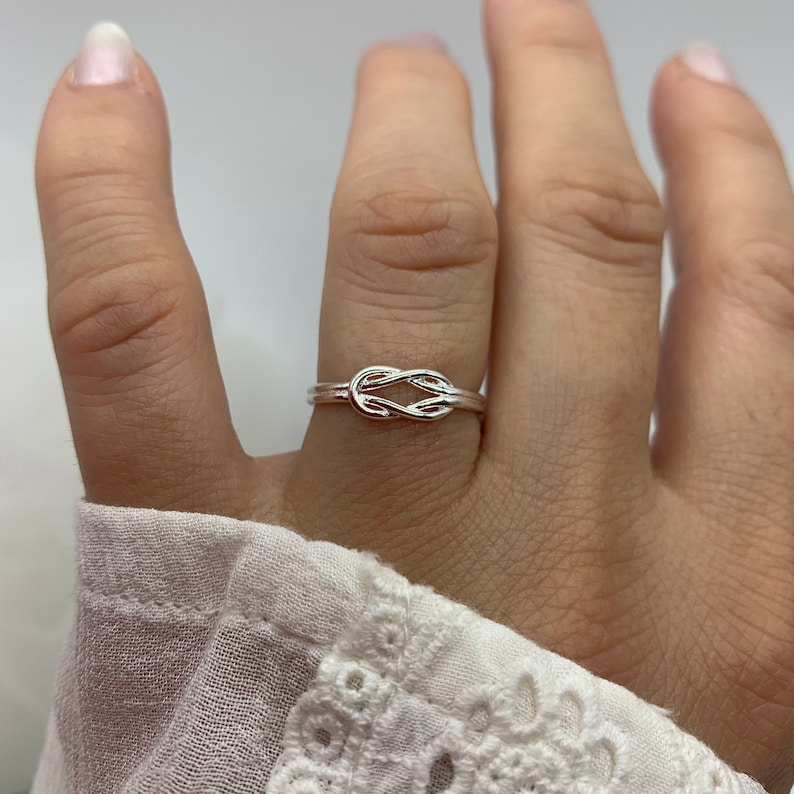 Op de afbeelding: Een zilveren knoop ring met een eenvoudig ontwerp. De ring wordt gedragen op de middelvinger van een hand.