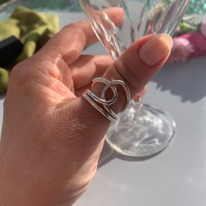 Op de afbeelding: Een zilveren ring met een uniek, gedraaid ontwerp. De ring wordt gedragen op de duim van een hand.